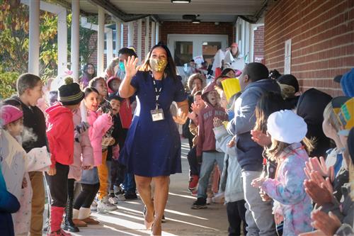 African American female in a gold mask walks outside down a breezeway with students cheering her on on either side